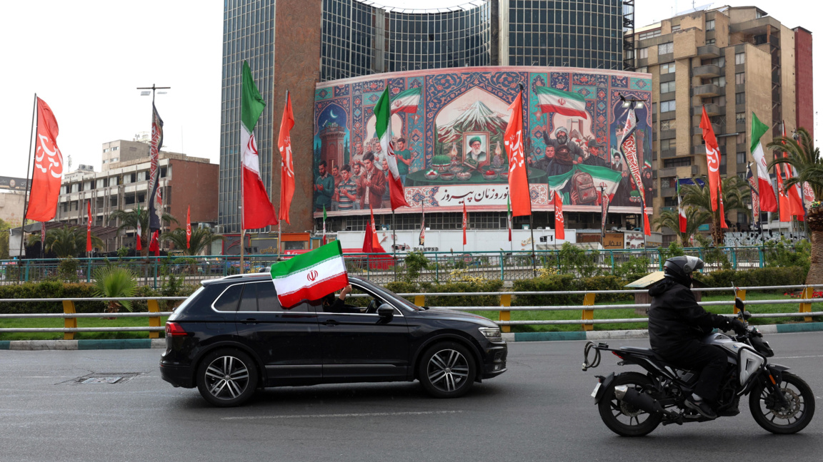 Кола, украсена с иранското национално знаме, минава покрай голям политически банер в Техеран, 31 март 2026 г.