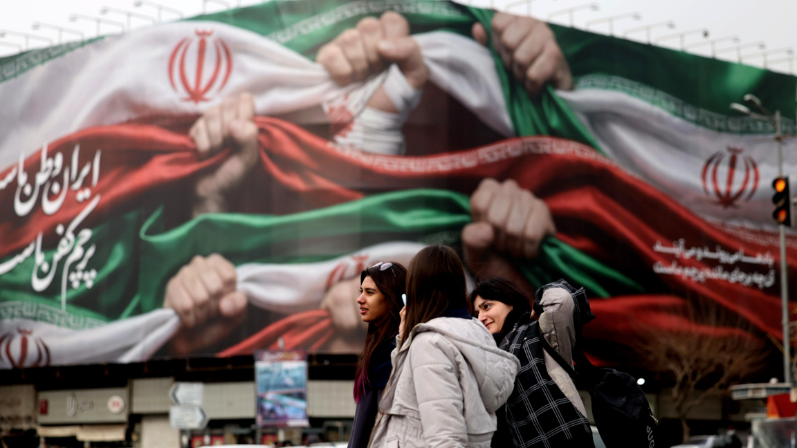 Момичета от Иран, заснети на 19 януари 2026г., докато минават покрай билборд в Техеран с надпис на персийски език, гласящ "Иран е нашата родина“.