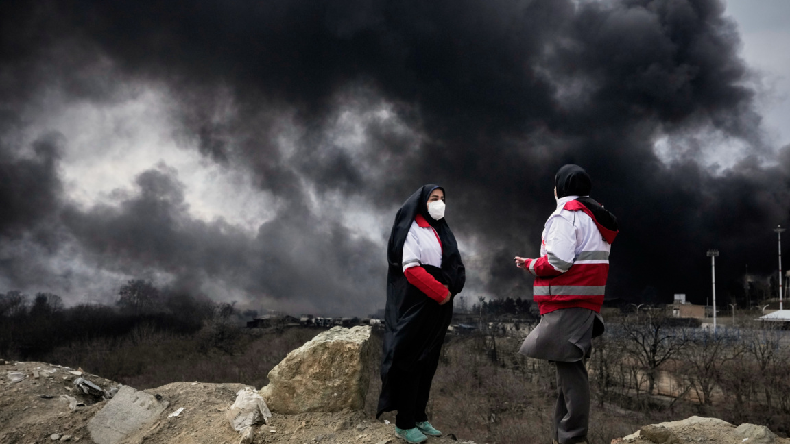 Иранки от Червения полумесец наблюдават гъстия дим, който се издига в небето над Техеран след въздушния удар през изтеклата нощ срещу петролно депо.