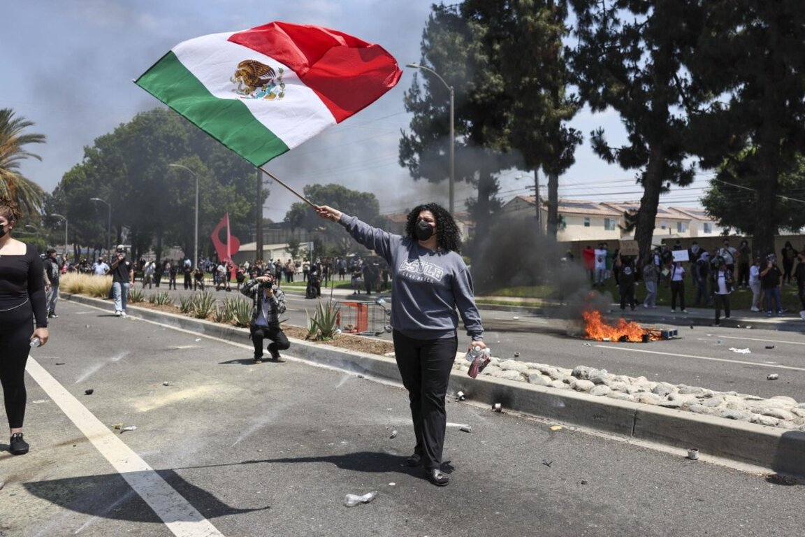 Протестираща развява мексиканския флаг на фона на сблъсъците.