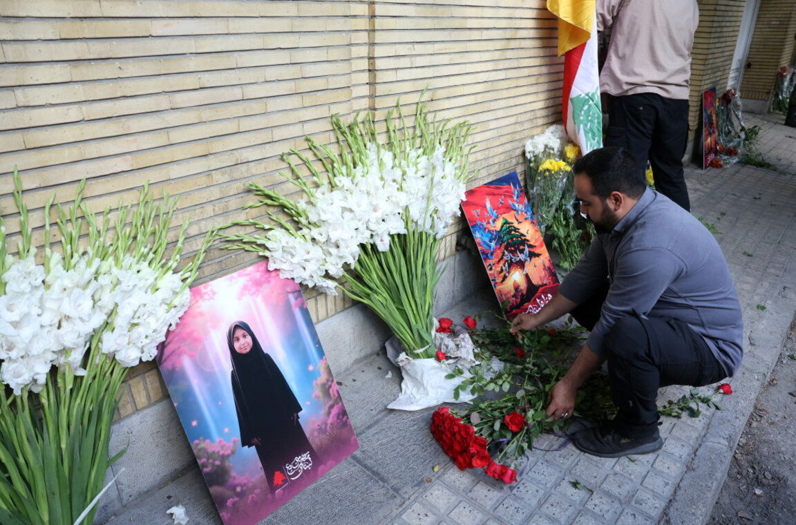 Жител на иранската столица поставя цветя пред ливанското посолство в памет на убитите при взривовете на пейджъри, сред които е момиченце (на портрета вляво), Техеран, 18 септември 2024 г.